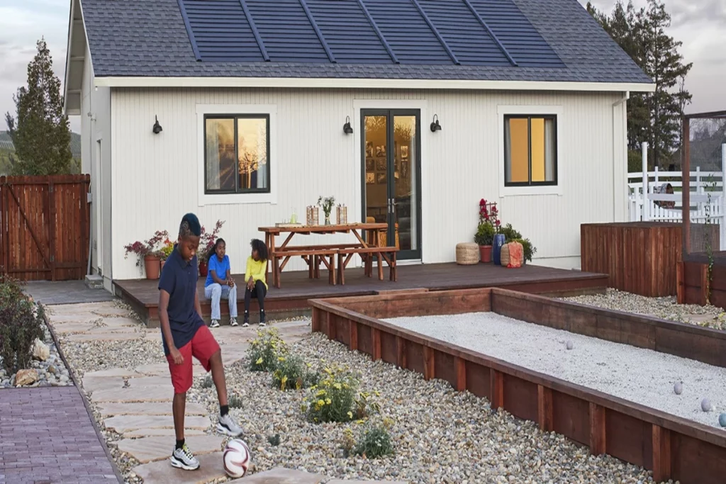 Children are playing in the yard with a house that has a roof made of Solar Shingles