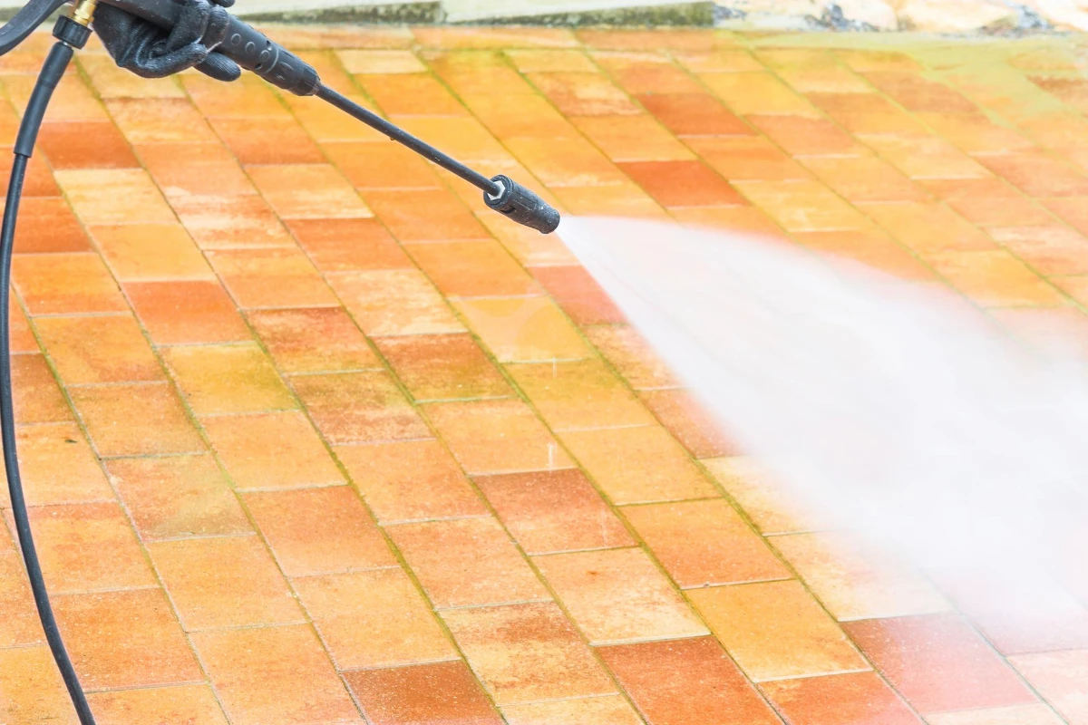 A person power washing a brick patio to remove dirt and grime.
