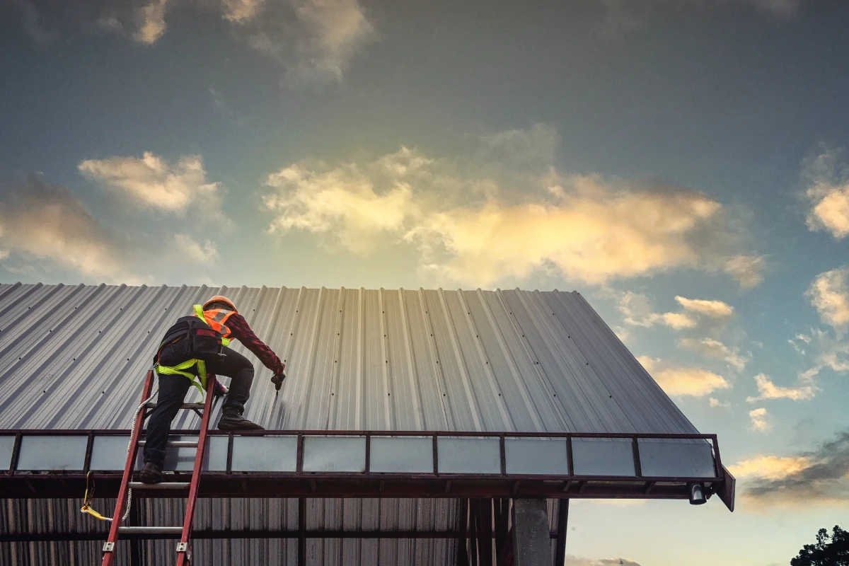 A man on a ladder working on a metal roof.