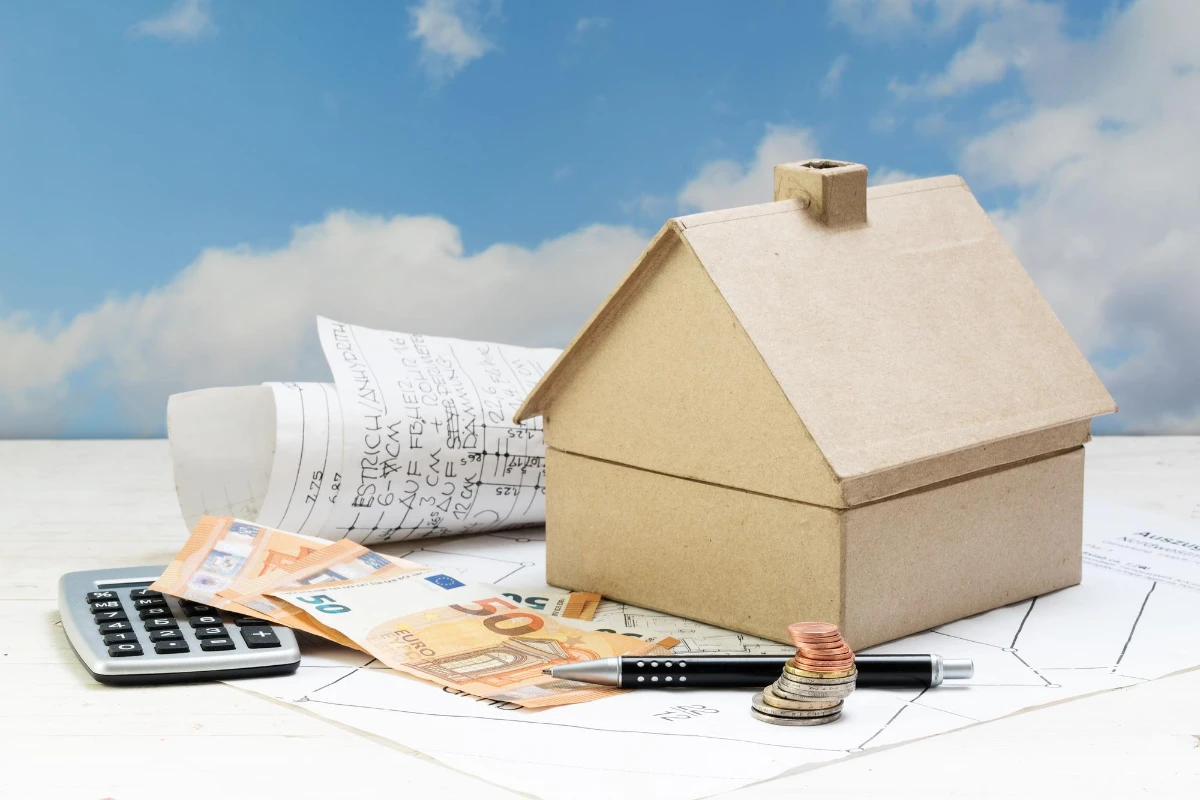 A house model, money, and a calculator on a wooden table symbolize financial planning for roof tax.