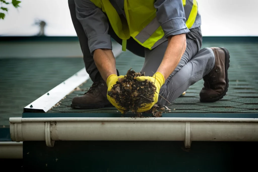 a man worker is cleaning a clogged roof gutter from dirt.