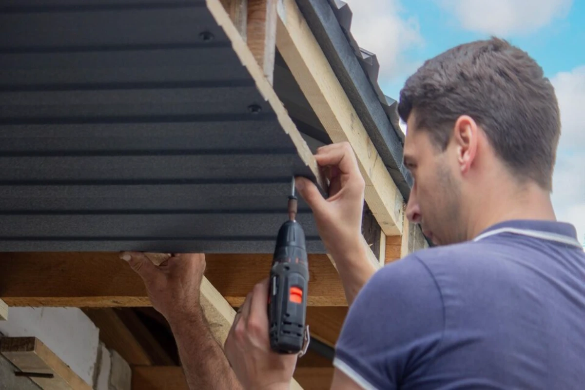 man repairs roof tightens selftapping screw with screwdriver selective focus