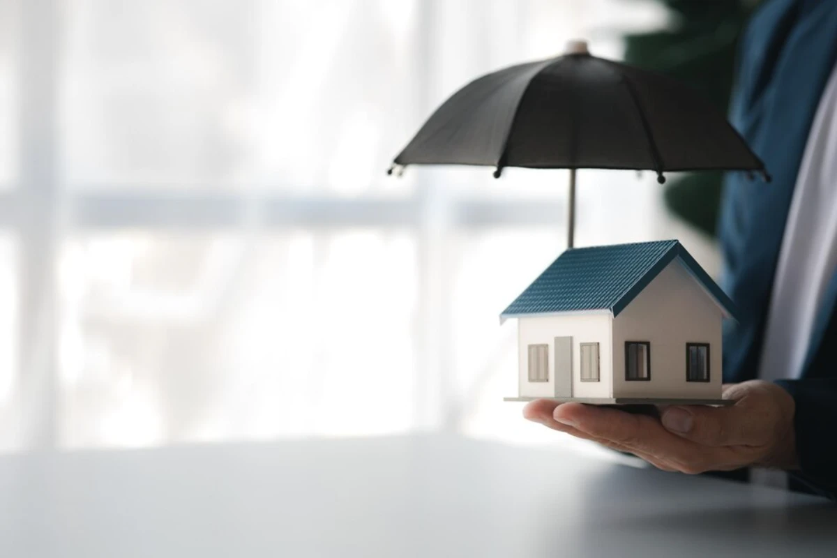 Individuals holding small umbrellas and model homes housing insurance against impending loss and fire building fire insurance home and real estate insurance concepts