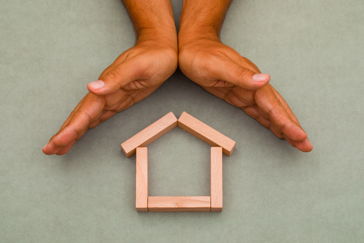 Hands enclosing wooden house. 